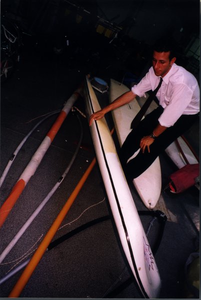 Homme en bras de chemise et cravate penché sur trois planches à voile.