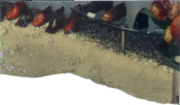 Chaussures alignées devant un mur blanc. Fragment déchiré.
