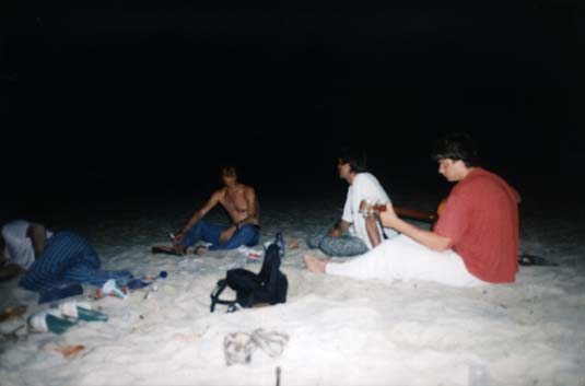 Joueur de guitare et jeunes hommes sur une plage la nuit .