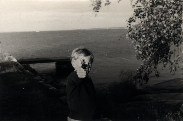 Enfant bras tendu avec une arme pointée de face. Noir et blanc.