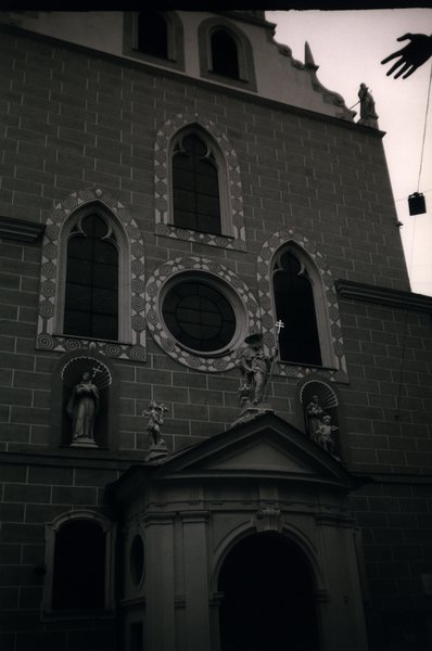 Façade d’église avec fenêtres en ogive et une main en avant-plan. Noir et blanc.
