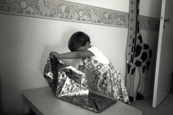 Enfant en robe pliant du papier cadeau sur une table. Noir et blanc.ᴬᴵ