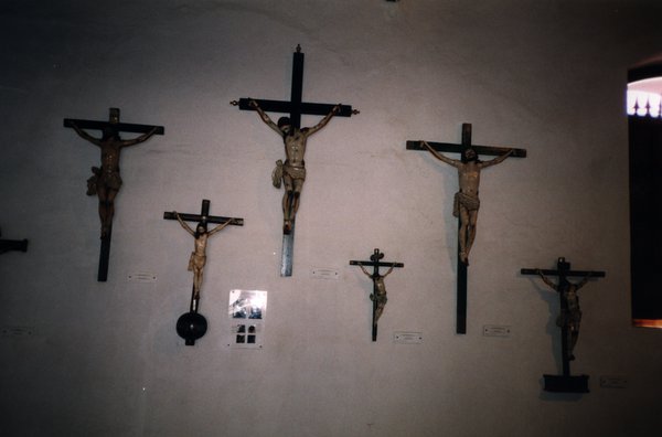 Grands et petits crucifix en bois avec Christ accrochés à un mur blanc.