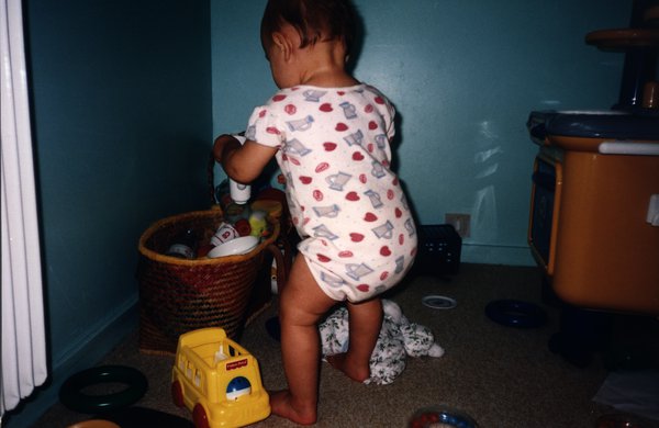 Petit enfant de dos debout en barboteuse avec des jouets.