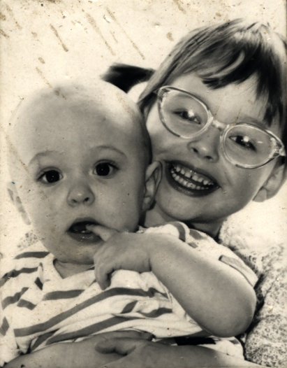 Petite fille souriante à lunettes et couettes avec un enfant à tee-shirt rayé dans les bras. Image avec rayures. Noir et blanc.
