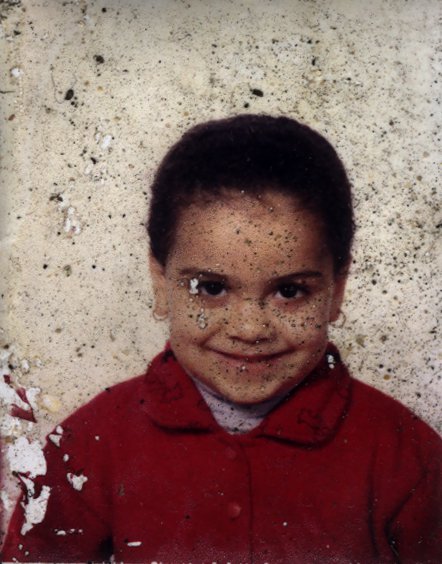 Enfant souriant de face en manteau rouge. Image très abîmée.