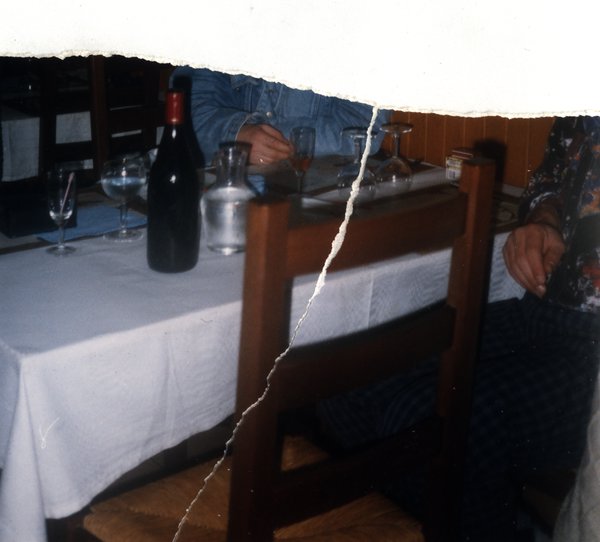Table de repas avec bouteille de vin et convives. Image avec déchirure, reconstituée.ᴬᴵ