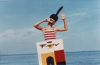 Petit personnage de la publicité Kodak en costume marin dans une embarcation en forme d’appareil photo, mer en arrière-plan.