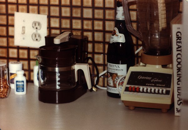 Meuble de cuisine avec une cafetière électrique, un mixer, une bouteille de vin et un livre de cuisine intitulé : « Great cooking ideas ».
