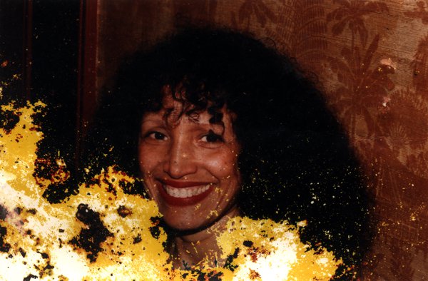 Visage de femme souriante à cheveux longs bouclés bruns. Image abîmée.