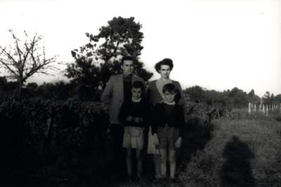 Homme, femme et deux jeunes garçons en bermudas posent au milieu d’un champ. Noir et blanc.