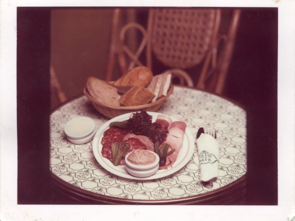 Table de bistrot avec couverts, assiette de charcuteries et corbeille à pain garnie.