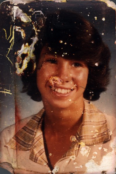 Portrait souriant d'une adolescente en chemise à carreaux. Image très abîmée.ᴬᴵ