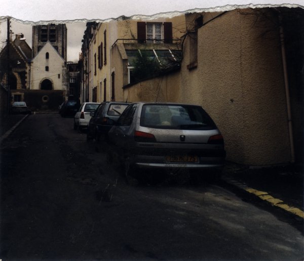 File de voitures garées dans une rue en montée. Image déchirée.