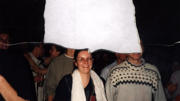 Femme à lunettes et écharpe blanche entourée d'un groupe, de nuit. Fragment déchiré.ᴬᴵ