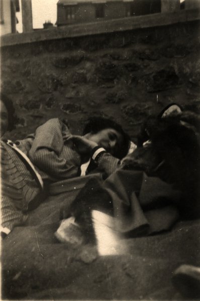Femme allongée contre un chien près d'un muret de pierre. Noir et blanc.ᴬᴵ