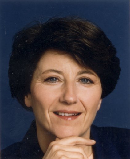 Visage de femme brune souriante, une main sous le menton.