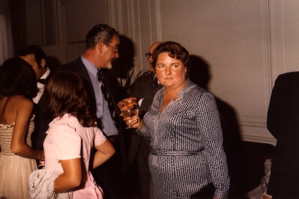 Groupe de personnes lors d'une réception, femme tenant un verre au premier plan.ᴬᴵ