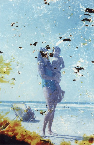 Femme portant un enfant sur une plage. Image fortement abîmée.ᴬᴵ