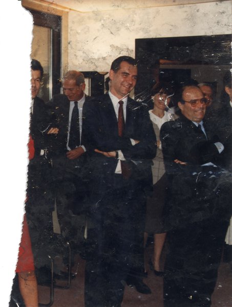 Hommes en complet et cravate debout bras croisés souriants. Image avec salissures.