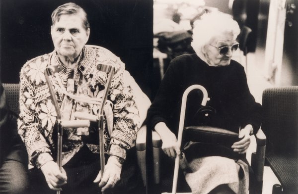 Homme âgé à chemise à motifs avec béquilles et vieille femmes avec canne blanche assis. Noir et blanc.