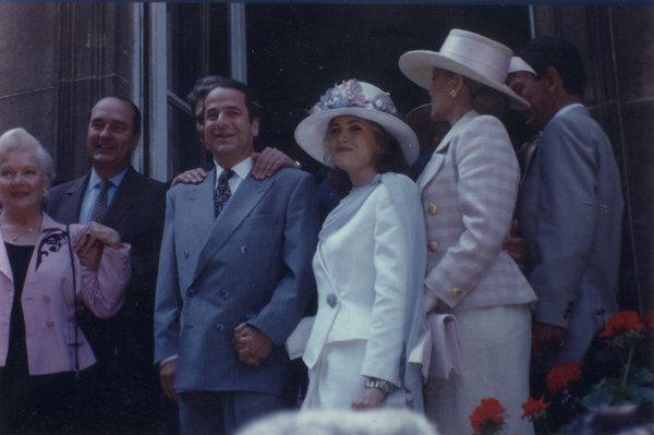 En haut d’un perron, Paul-Loup Sulitzer souriant la main dans celle d’une jeune femme en tailleur blanc et chapeau, entouré par Jacques Chirac et Line Renaud.