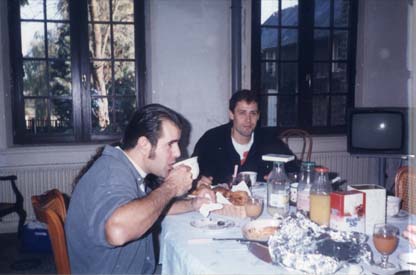 Deux hommes bruns attablés devant un petit déjeuner, grandes fenêtres en arrière plan.