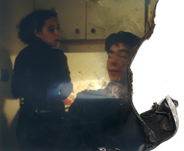 Cuisine avec jeune fille debout et personne assise. Image endommagée.