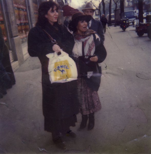 Deux femmes debout en manteaux dans la rue avec des sacs plastiques dans les mains.