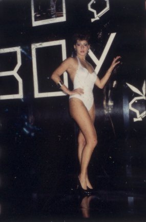 Femme en maillot de bain blanc posant devant une enseigne « BOY » dans une boîte de nuit.ᴬᴵ