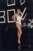 Femme en maillot de bain blanc posant devant une enseigne « BOY » dans une boîte de nuit.ᴬᴵ