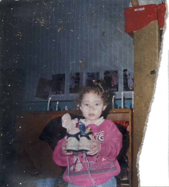 Petite fille avec paire de baskets dans les mains, bougies allumées en arrière-plan.