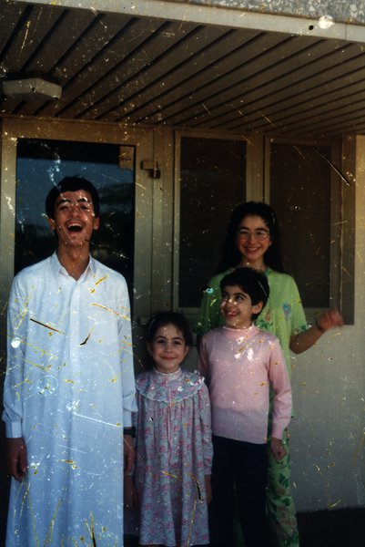 Homme, deux fillettes et une femme couverts de confettis devant une maison.ᴬᴵ