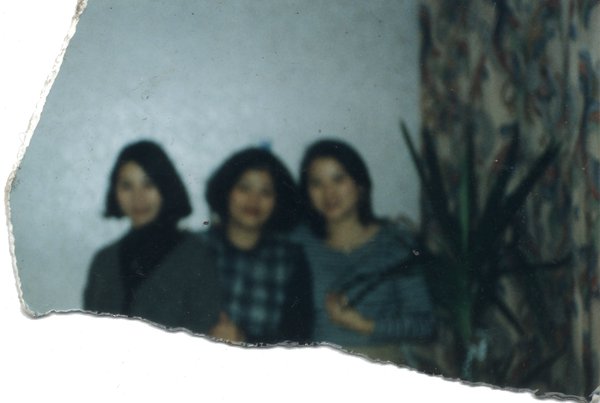 Trois jeunes femmes posant debout près d’une plante verte. Fragment.
