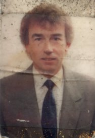 Visage d’homme à cheveux clairs en costume gris et cravate. Image avec pliure.