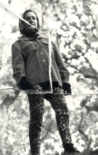 Femme blonde debout avec pantalon fuseau à motif léopard, arbres en arrière-plan. Image avec pliures. Noir et blanc.