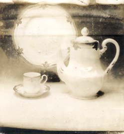 Théière blanche en porcelaine, une tasse, et une assiette. Noir et blanc.