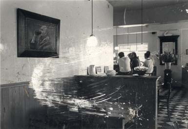 Salle de restaurant, en arrière-plan individus accoudés au comptoir. Noir et blanc. Image avec rayures.