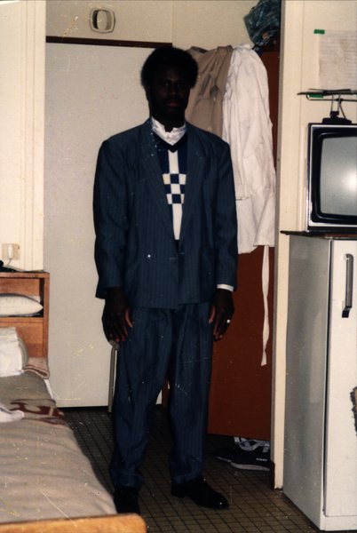 Homme en costume à rayures dans une chambre, télévision en arrière-plan.ᴬᴵ