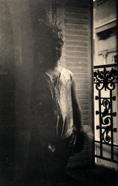 Personne en ombre près d'une fenêtre à balcon en fer forgé, coiffée d'une parure. Noir et blanc.ᴬᴵ