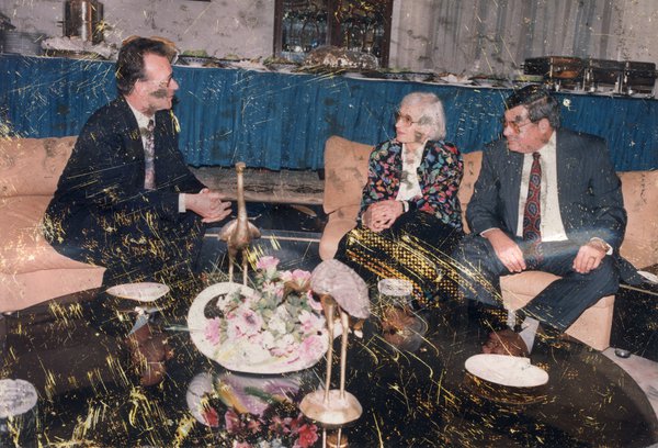 Deux hommes et une femme assis sur des canapés face à une table basse noire, buffet de cocktail en arrière-plan.