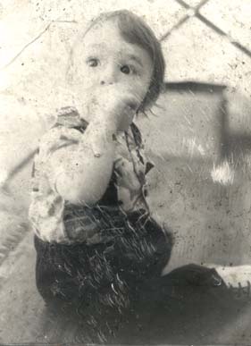 Gros plan d'un bébé assis par terre, la main à la bouche. Noir et blanc.ᴬᴵ