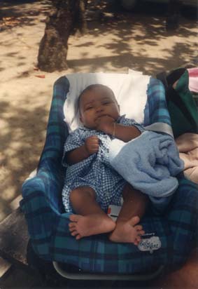 Petit enfant assis dans un siège bébé de voiture posée à terre, ombres en arrière-plan.