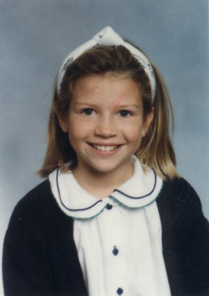 Visage de petite fille blonde souriante à bandeau dans les cheveux et chemise blanche à collerette.