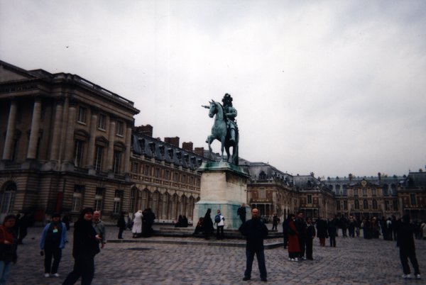 Homme devant la statue de Louis XIV dans la cour pavée du château de Versailles.