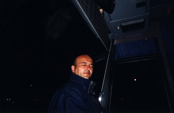 Homme debout en blouson les yeux fermés.