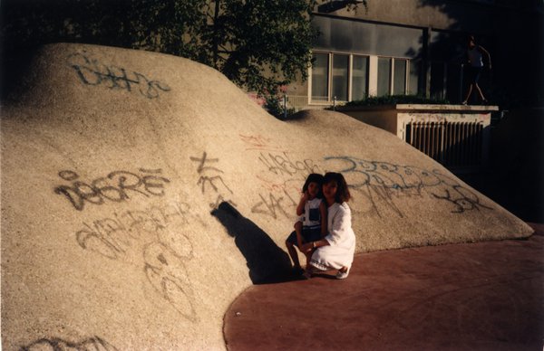 Une femme et sa petite fille accroupies devant un terre-plein en forme de dune recouvert de tags.