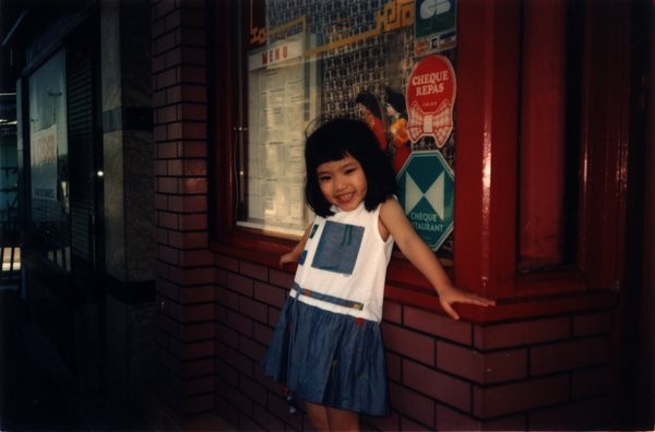Petite fille souriante debout devant la façade d’un restaurant.