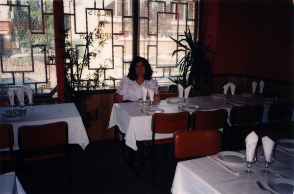 Femme brune en chemisier blanc assise à une table de restaurant.