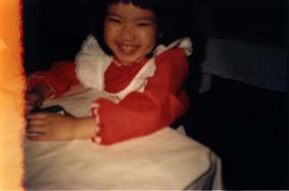 Petite fille souriante assise en robe rouge et blanche. Trace d’amorce.